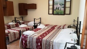 Habitación de hotel con tres camas, cada una con una colcha estampada en rojo y blanco y toallas blancas dobladas con cuidado. Hay un mueble de madera sobre las camas y un cuadro en la pared.