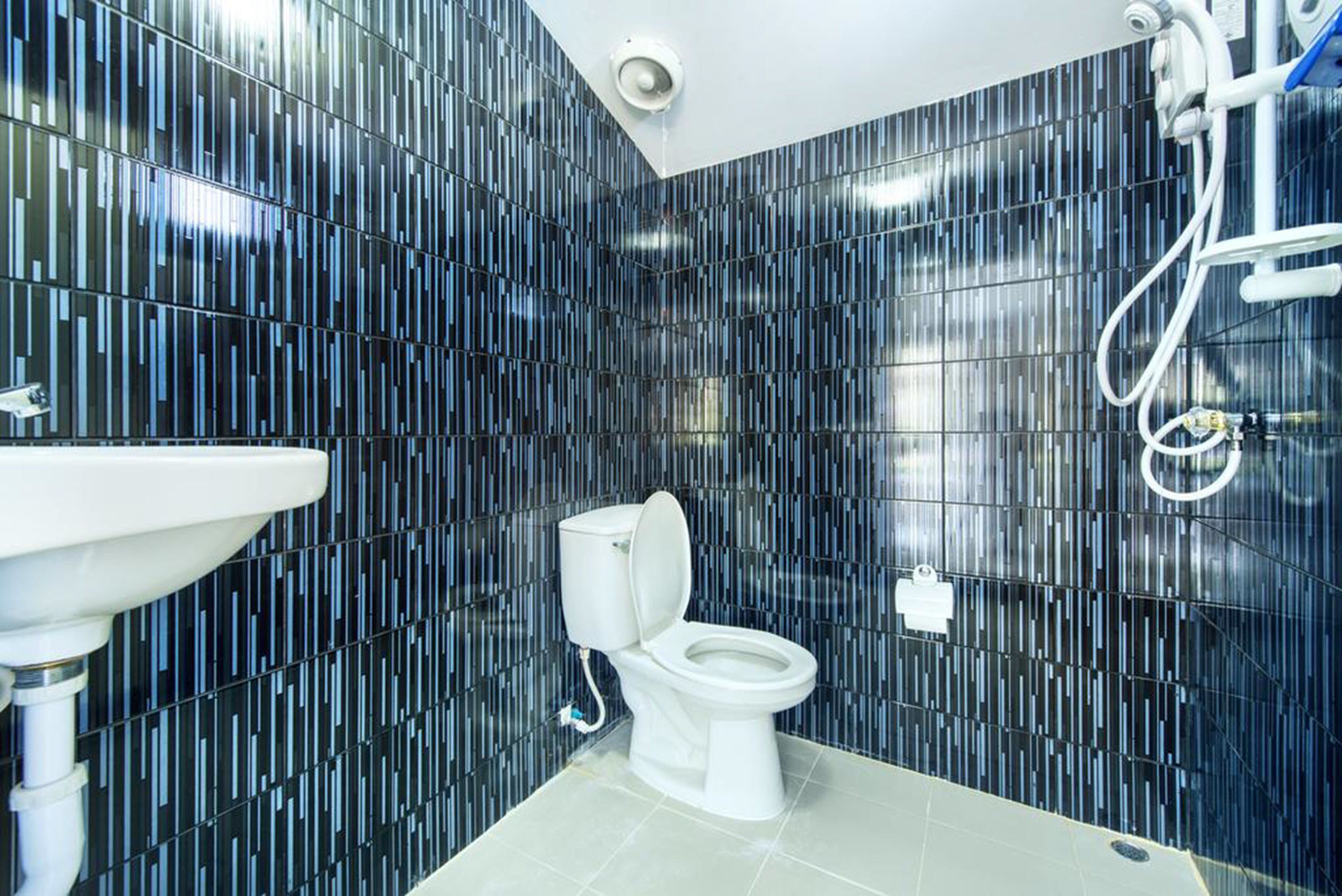 Un baño moderno con pared de azulejos negros, un inodoro blanco y un lavamanos blanco.