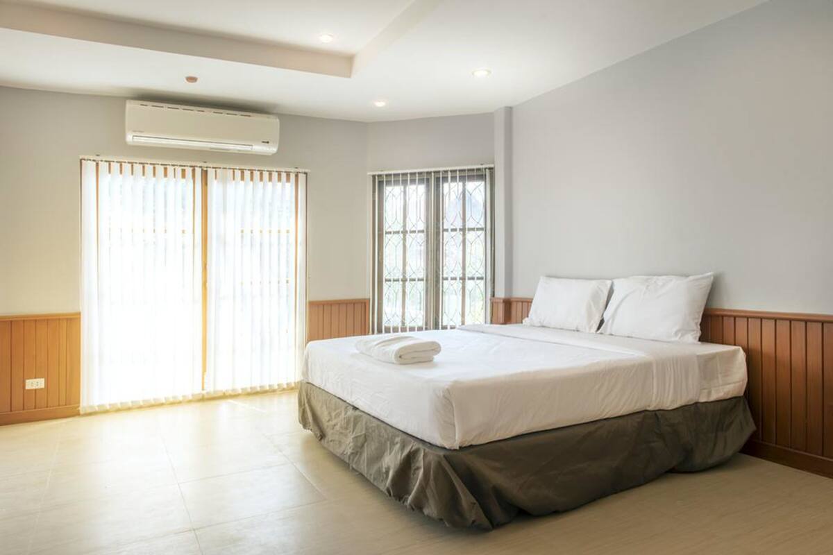 A hotel room with a large bed, a window with metal bars, an air conditioning unit, and wooden paneling on the walls.