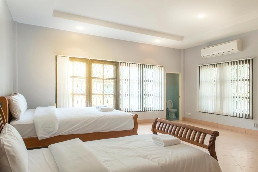 A hotel room with two beds, a bench, and a window with blinds.