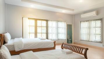 A hotel room with two beds, a bench, and a window with blinds.