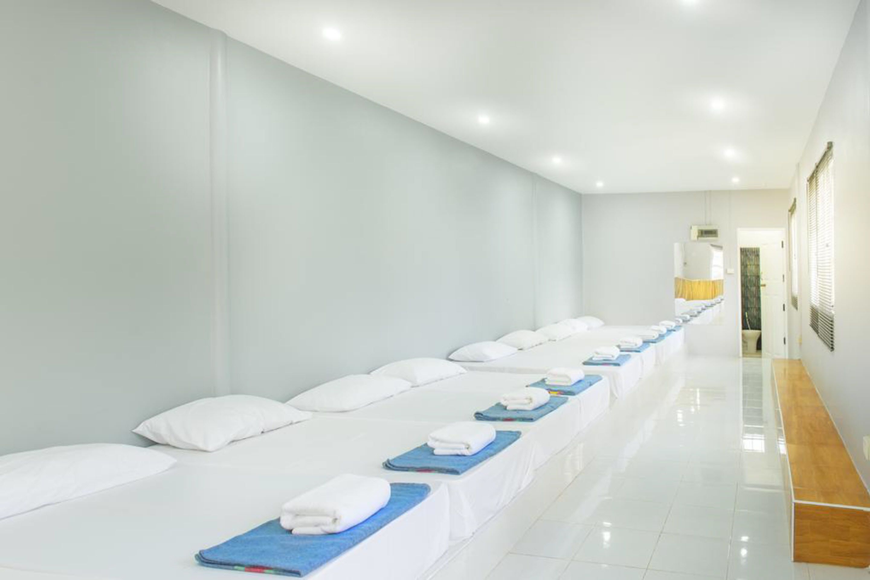 A hotel room with multiple beds aligned in a row, each with white bedding and blue towels.