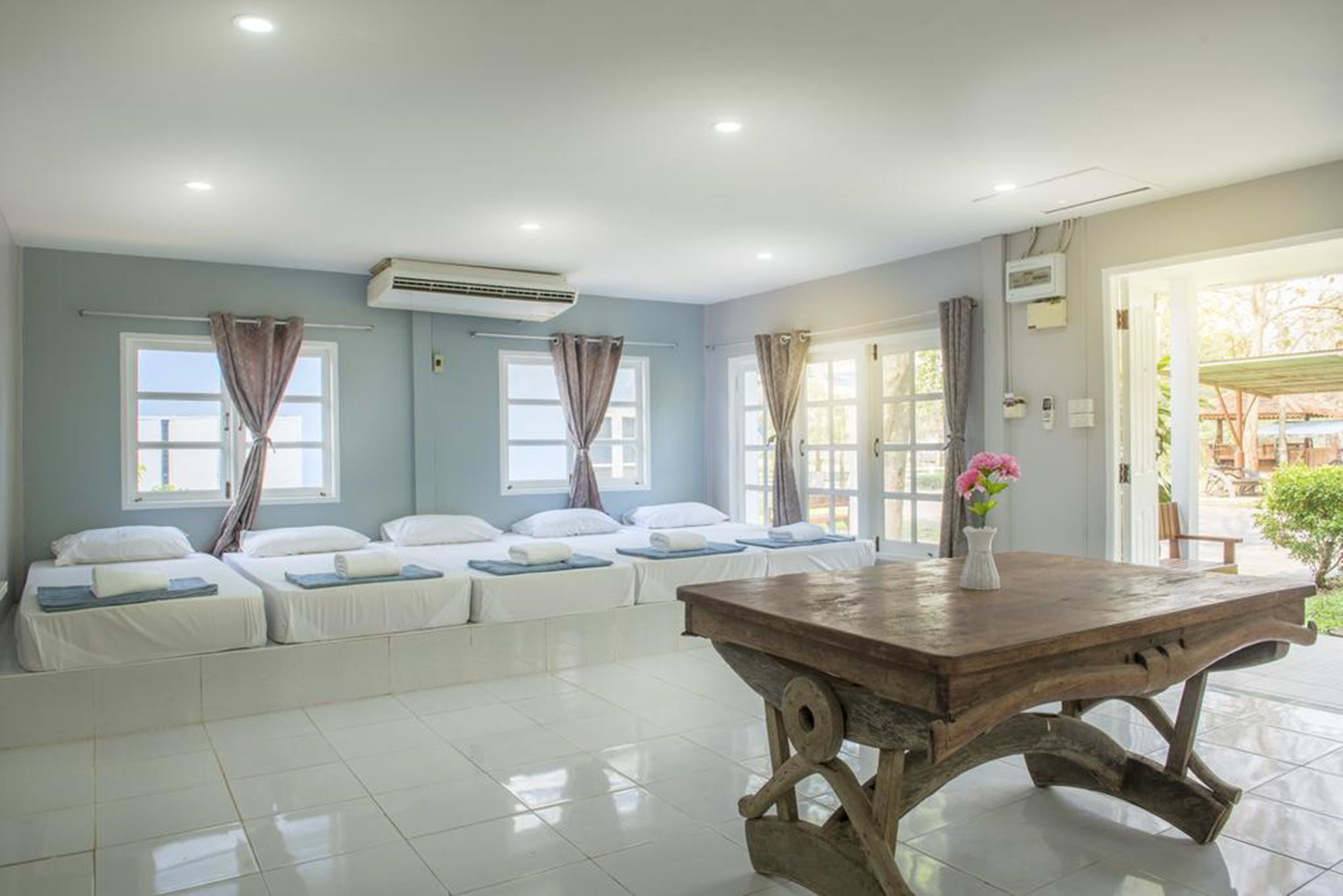 A hotel room with a long bed, a wooden table, and a window with curtains.