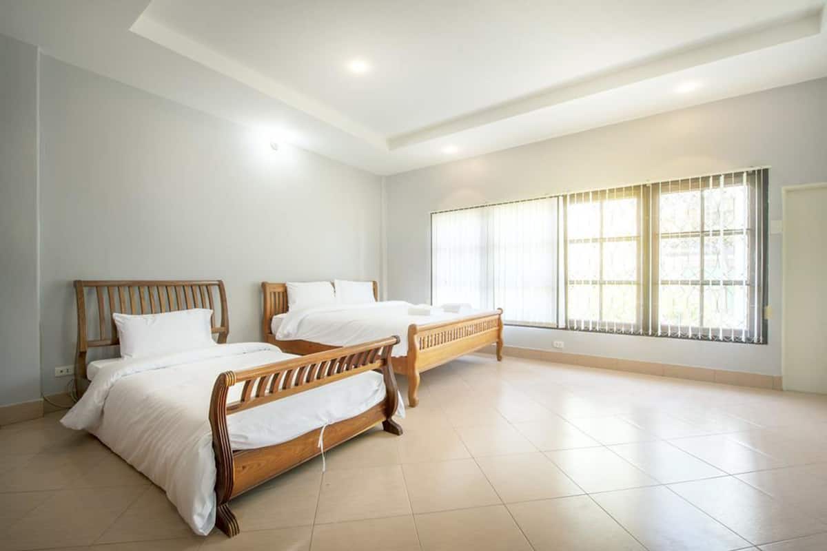 A hotel room with two wooden beds, white bedding, a large window with blinds, and a tiled floor.