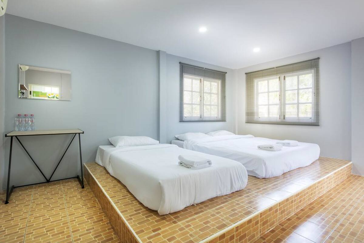 A hotel room with two beds, a small table, a mirror, and a window with blinds.