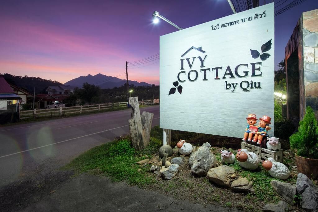 Qiu-nimimerkillä varustettu kyltti, joka on sijoitettu Ivy Cottage -mökin yhteyteen. Kyltin taustalla on maalaismaisema, johon kuuluu kiviä ja koristehahmoja.