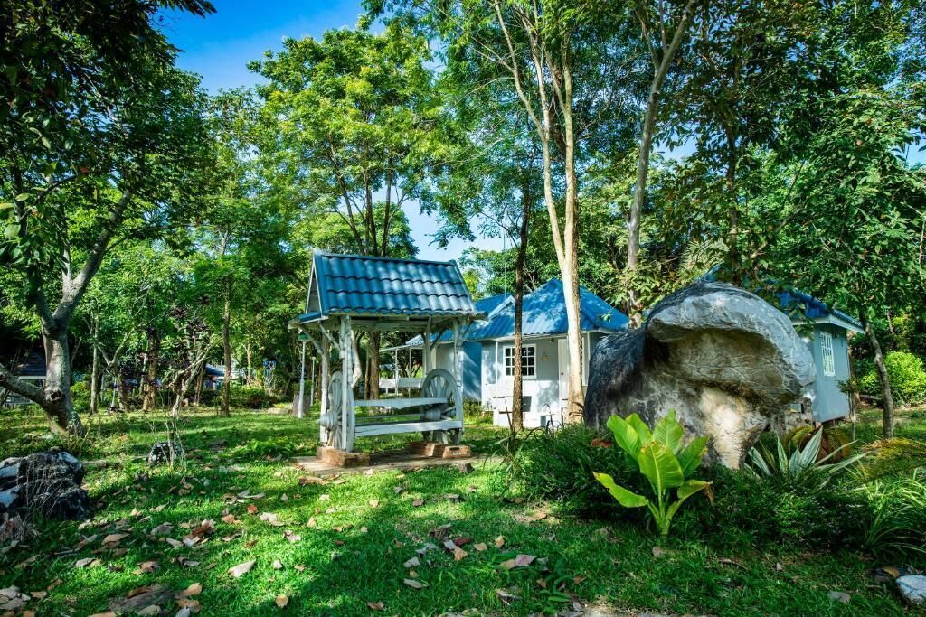 A rustic wooden structure with a blue roof, surrounded by lush greenery and trees.