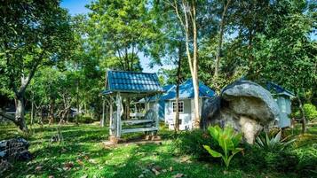 A rustic wooden structure with a blue roof, surrounded by lush greenery and trees.