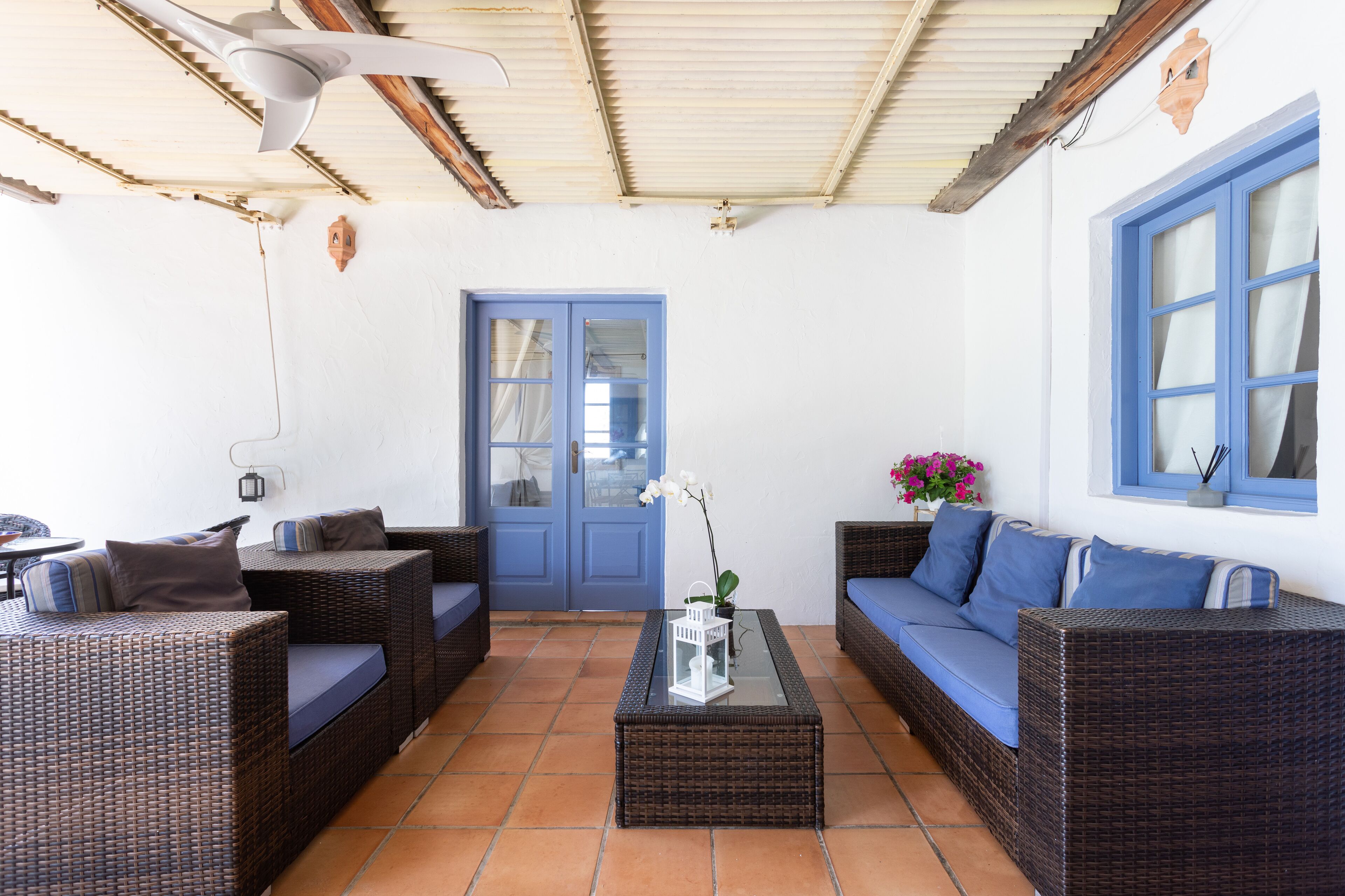 Une pièce meublée de mobilier en osier, avec une porte bleue et un mur blanc.
