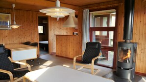 A cozy room with a wooden interior, a table, two chairs, a sofa, a fireplace, and a window with curtains.