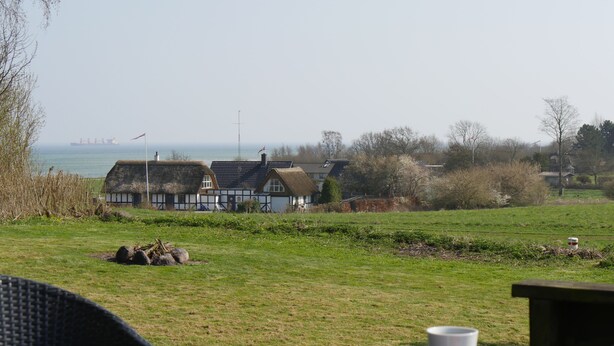 A table with a cup and a plate of food, a grassy field, and houses in the background.