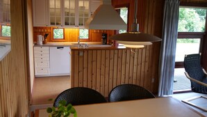 A wooden cabin interior with a dining area, kitchen, and a large window.