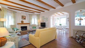 Ein gemütliches Wohnzimmer mit einer Couch, Sesseln, einem Kamin, einem Fernseher und einem Essbereich mit Tisch und Stühlen.