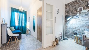 Ein modernes Wohnzimmer mit einem blauen Sofa, einem weißen Sessel und einem kleinen Tisch. Eine Ziegelwand mit Bilderrahmen und Lampe.