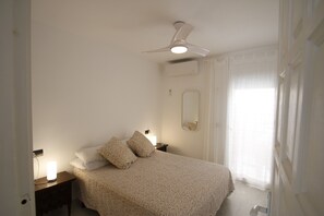Ein Schlafzimmer mit einem Bett, Nachttischlampen, einem Deckenventilator und einem Fenster mit Vorhängen.