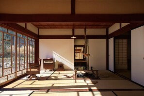 A traditional Japanese room with tatami flooring, a low wooden table, a small stool, a radio, and a sliding door leading to another room.
