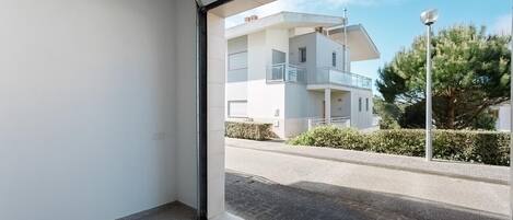 Un appartement moderne doté d’une grande fenêtre, d’un balcon et offrant une vue sur une rue résidentielle.