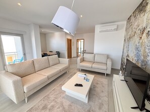 A modern living room with a sofa, armchair, coffee table, and TV. - Serene Horizon - BY SCH (Nazaré)