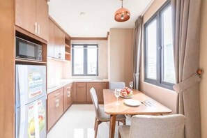 A compact kitchen with wooden cabinets, a refrigerator, and a dining table set for two.