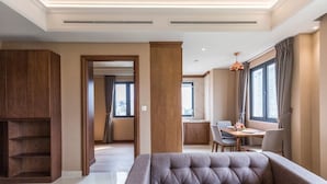 Uma sala de estar moderna com um sofá seccional, armários de madeira, um espaço de jantar com mesa e cadeiras, e grandes janelas com cortinas.