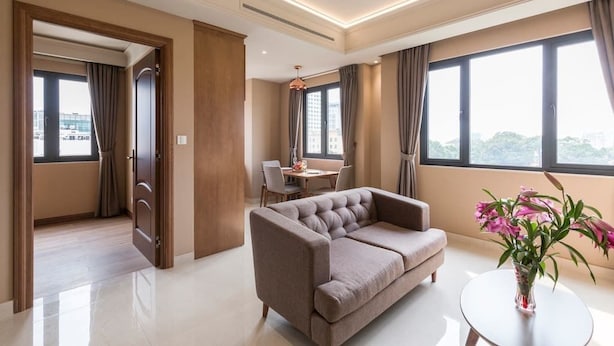 Quarto de hotel moderno com sofá, mesa de jantar e amplas janelas com vista para a cidade.