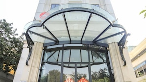 Entrada imponente de um hotel, com porta de vidro e tapete vermelho.