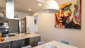 Eine moderne Küche mit Edelstahlgeräten, einem weißen Esstisch mit Schüssel und einem farbenfrohen abstrakten Gemälde an der Wand.