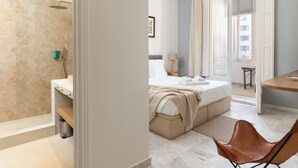 Ein modernes Hotelzimmer mit Dusche, einem Bett, einem Schreibtisch und einem Sessel.