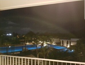 A nighttime view of a hotel with a swimming pool, palm trees, and a building with lights. - The Sea Condominium A22 (Sam Roi Yot)