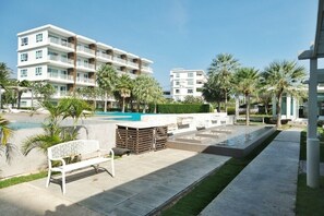 A modern hotel with a swimming pool, palm trees, and a white bench. - The Sea Condominium A22 (Sam Roi Yot)