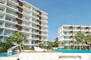 A hotel with multiple balconies, a swimming pool, and palm trees. - The Sea Condominium A22 (Sam Roi Yot)