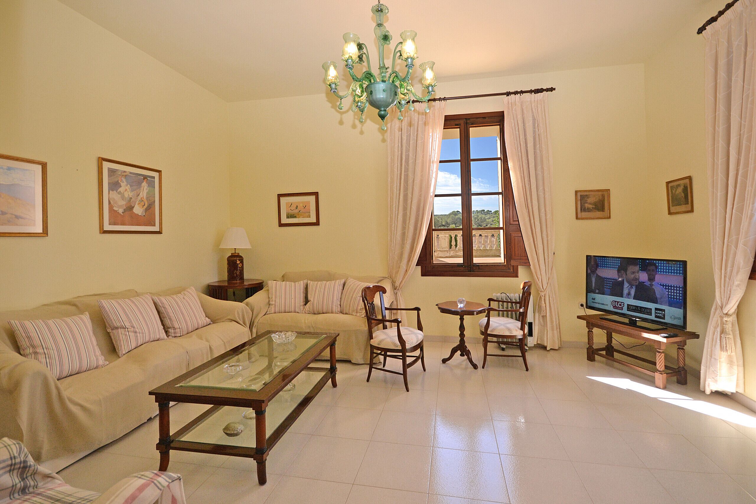 Una sala de estar con un sofá, sillas, una mesa de centro, un televisor y una ventana con cortinas.