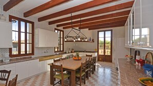 A spacious kitchen with wooden beams, a large dining table, and a view of the outdoors.