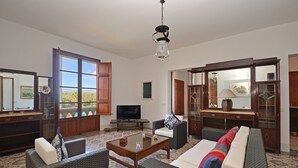 A spacious living room with wicker furniture, a television, and large windows offering a view.