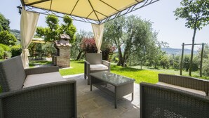 Eine Terrasse im Freien mit Korbmöbeln, einem Glastisch und einem Kamin aus Stein.