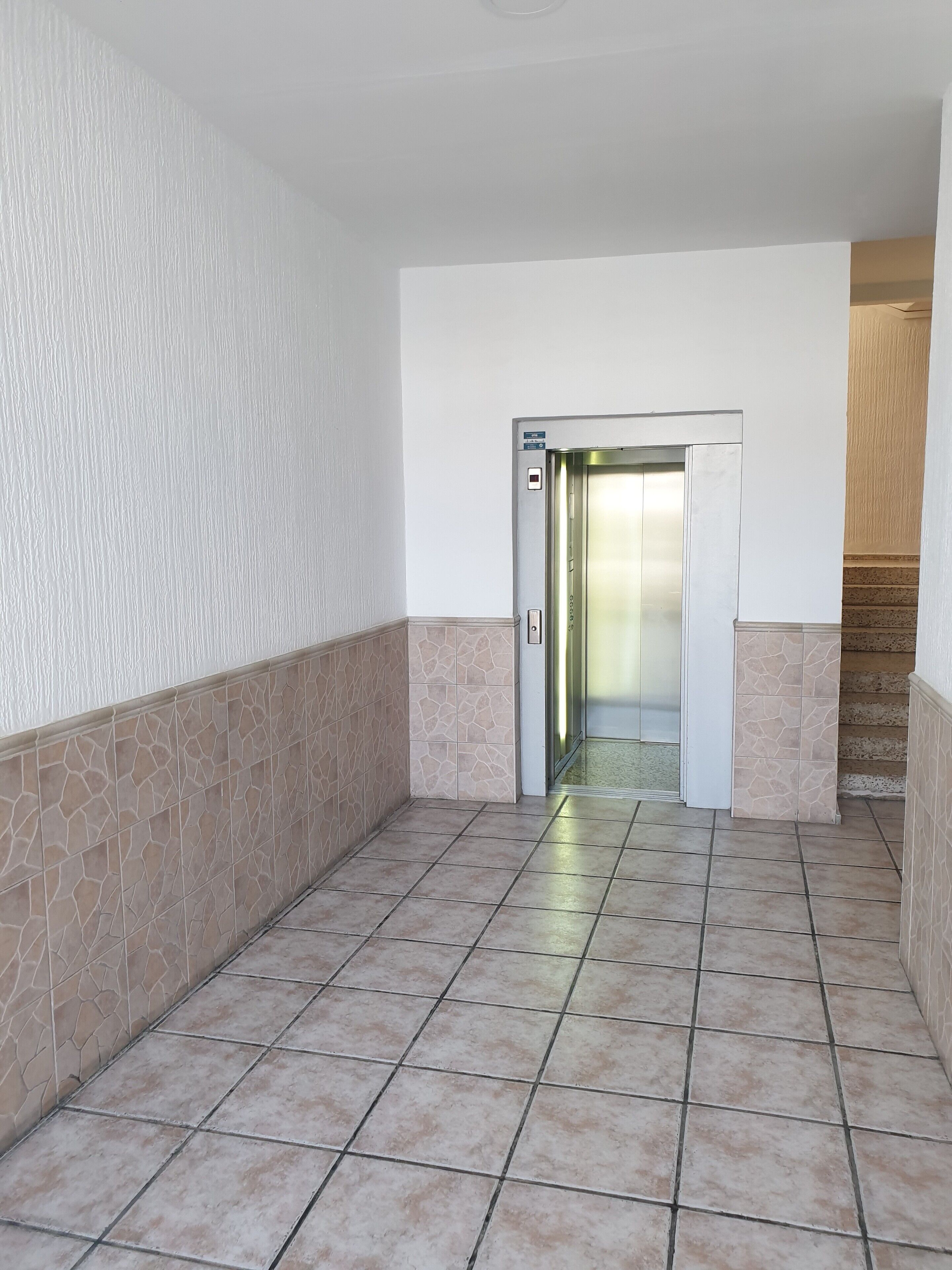 A hallway with a tiled floor, a door leading to an elevator, and a staircase to the right.