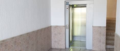 A hallway with a tiled floor, a door leading to an elevator, and a staircase to the right.