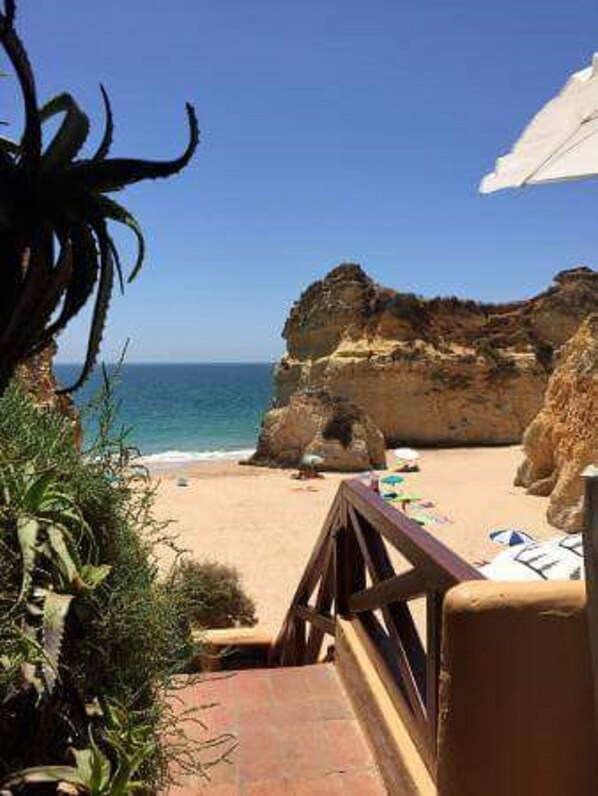 A beach view with a rocky cliff, a wooden deck, and a clear sky.