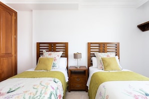 A hotel room with two beds, wooden headboards, floral bedding, a nightstand with a lamp, and a wardrobe.
