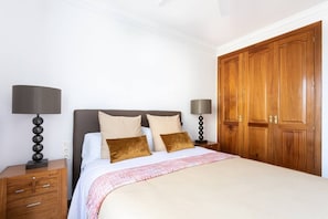 Un dormitorio con una cama, dos mesitas de noche con lámparas, un armario de madera y una pared blanca.