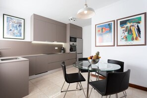 A modern kitchen with a dining area, featuring a glass table and black chairs.