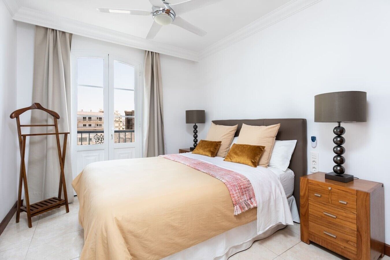 A hotel room with a bed, bedside tables, a wardrobe, a hanging rack, and a view of the city through the window.