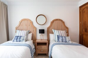 Habitación doble con dos cabeceros de madera, una mesita de noche con lámpara y un espejo redondo en la pared.