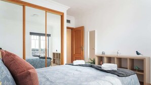 Ein Schlafzimmer mit Bett, Kleiderschrank, Schreibtisch und einer Regalreihe mit Dekoration.