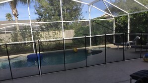 Une piscine extérieure couverte, protégée par une structure en verre, entourée de chaises longues et d’une clôture en bois.