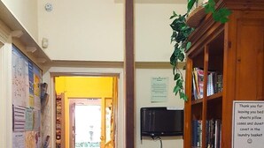 A hallway with a wooden bookcase, a television, and a sign thanking guests for leaving bed sheets and pillows in the laundry basket. - Rucksacker Backpacker Hostel (Christchurch)