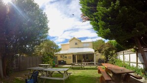 A backyard with picnic tables and benches, a wooden fence, and a house with a covered porch. - Rucksacker Backpacker Hostel (Christchurch)