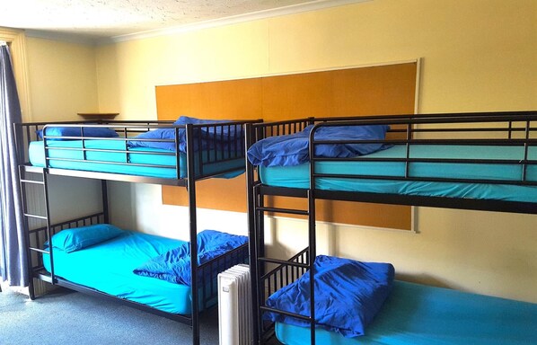 A dormitory room with bunk beds, a radiator, and a window with curtains.