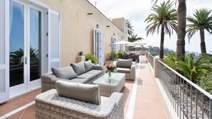 A balcony with wicker furniture, a railing, and palm trees.