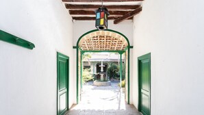 A corridor with a tiled floor leading to a building entrance with a green door and an archway.
